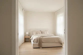 Chambre peinte en blanc cassé avec parquet clair et literie en lin neutre pour agrandir visuellement l'espace